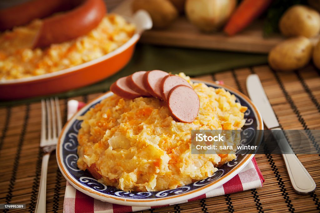 een bord met hutspot met plakjes rookworst erop